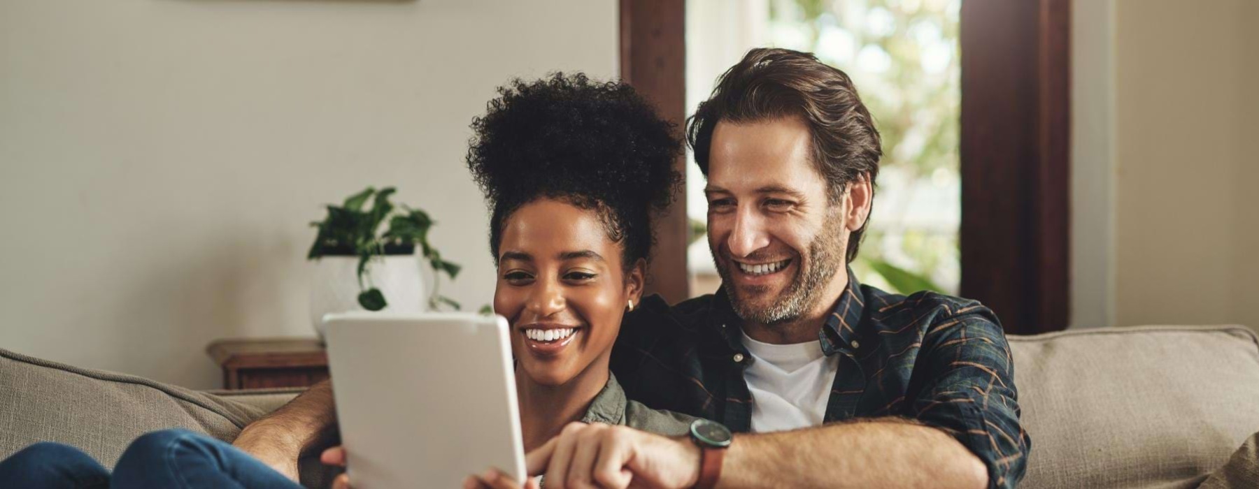 husband and wife look at a tablet while sitting on couch